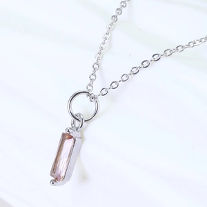Macro shot of rectangular champagne zircon pendant on a silver necklace with white fabric background