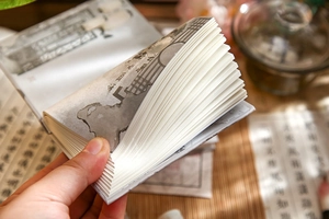 Close-up of hand flipping thick white pages of a mini A7 notebook with ink art theme