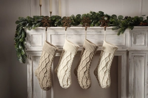 Close-up of four knitted Christmas stockings with cable patterns hanging on fireplace