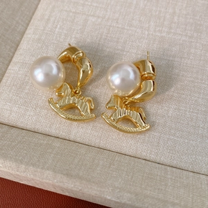 Détail de boucles d'oreilles cheval à bascule dorées avec perles sur écrin beige
