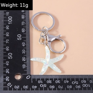 Detail shot of white glitter starfish keychain with silver metal ring on ruler scale