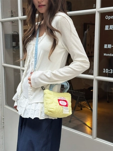 Quilted yellow nylon crossbody bag with heart patch and light blue strap on a model
