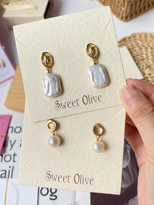 Detailed view of vintage baroque pearl earrings with golden coin charms on display card
