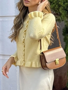 Detail of yellow knit cardigan with ruffle trim and brown leather shoulder bag with lock