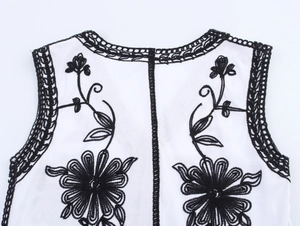 Detailed close-up of white vest featuring black floral embroidery and lace edges