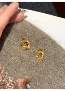 Detailansicht goldener ovaler Ohrringe mit schimmernder Froststruktur auf grauem Stoff