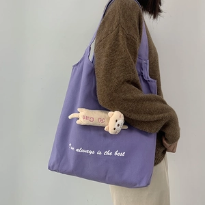 Detail of purple canvas tote bag with plush cat charm shown on model shoulder