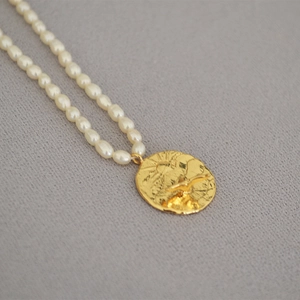 Detailed close-up of a vintage gold coin pendant featuring bird relief on freshwater pearls