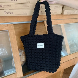Dettaglio della borsa shopper nera trapuntata con texture a bolle e logo bianco