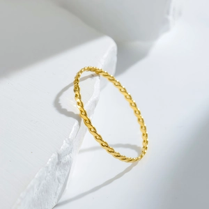 Elegant twisted rope design gold-plated stainless steel ring on white stone background