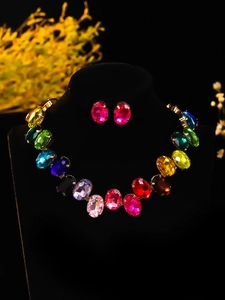 Detailed view of colorful oval crystal necklace and stud earrings set on black velvet stand