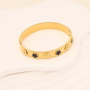 Dettaglio del bracciale rigido dorato in acciaio inossidabile con quadrifogli neri e fiori