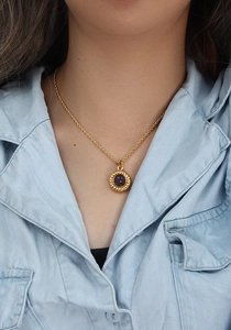 Gros plan d'un collier doré avec pendentif en agate violette sur une chemise en jean bleu