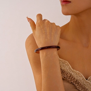 Macro shot of a dark amber acrylic resin round bangle on a wrist, showing texture