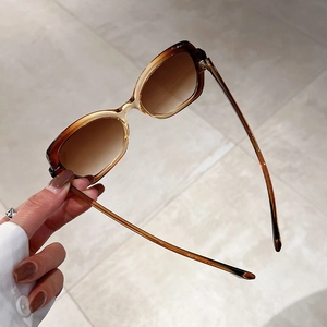 Handheld tortoiseshell sunglasses with brown gradient lenses on marble background