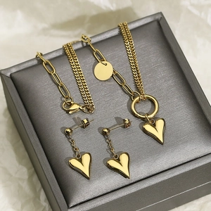 Detail shot of golden double-layer heart necklace and matching earrings in a gray box