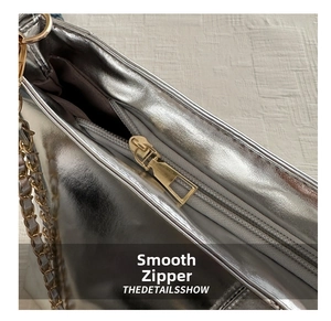 Macro view of smooth gold zipper and silver metallic chain on a large tote bag