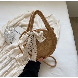 Detail of round straw handbag with a white lace bow, pearl buckle and top handles