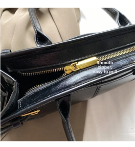 Detail of smooth gold zipper closure on black leather tote bag with metallic hardware