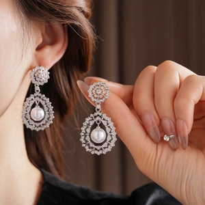 Detail of silver drop earrings with zircons and a white pearl on a model's ear