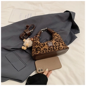 Close-up of leopard print shoulder bag with plush pendant on grey blazer fabric