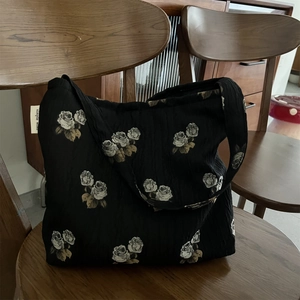 Detail of black textured jacquard tote bag with white rose patterns and simple wish label