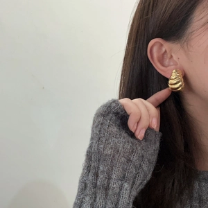 Detailed close-up of a golden spiral geometric earring worn by a model in soft light