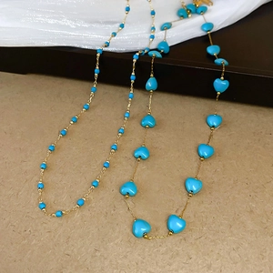 Detailed shot of bohemian gold chains with round and heart-shaped turquoise blue beads