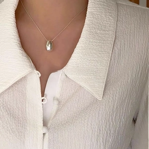 Close-up of a polished silver teardrop pendant necklace worn on a white textured shirt