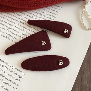 Detail view of burgundy plush hair clips set featuring golden metal B logos and soft texture
