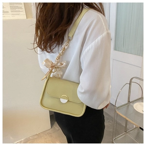 Detail of light yellow leather crossbody bag featuring a silk scarf and metal magnetic clasp
