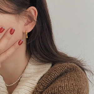 Close-up of minimalist gold beaded hoop earrings worn by a model in winter knitwear