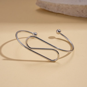 Detail of silver minimalist geometric open bangle with round beads on beige background