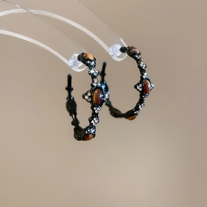 Macro detail of black metal hoop earrings with amber stone and sparkling crystals