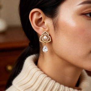 Detail of gold floral pearl earrings with zircon droplets worn by model in soft lighting
