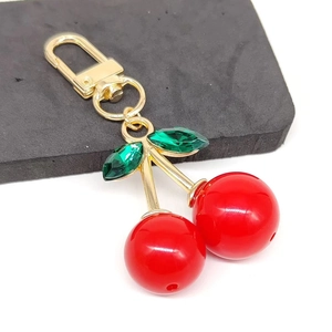 Detailed view of red cherry keychain with green faux gemstone leaves and golden clasp