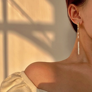 Elegantes pendientes largos de oro con perlas barrocas en una modelo bajo la luz solar