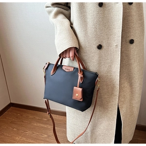 Detail of nylon tote bag featuring brown leather handles and brand logo tag