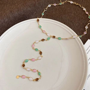 Macro shot of gold necklace with colorful oval gemstones on a white ceramic plate