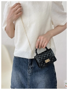 Close-up of black jelly bag featuring gold chain strap and bead handle on model