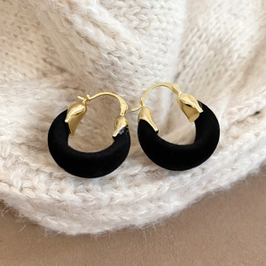 Macro view of gold metal hoop earrings with black velvet texture on a knit background