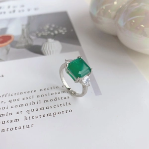 Detail view of emerald-cut green stone ring with water-drop side diamonds on silver band