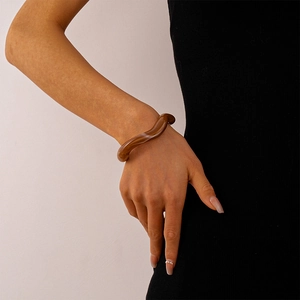 Detail of a wavy brown acrylic cuff bracelet with marble texture worn by a model