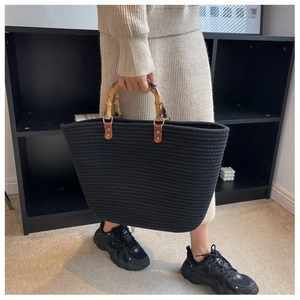 Detailed view of woven black tote bag with natural bamboo handles held by a model