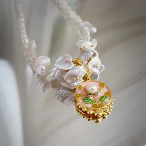 Detail of hand-painted floral enamel pendant with baroque pearl necklace on mirror surface