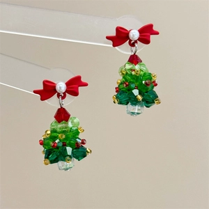 Detailed close-up of handmade beaded Christmas tree earrings with a red bow and pearls