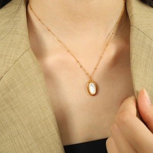 Golden necklace with white oval shell pendant worn by a model in professional styling