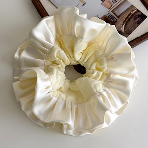 Detail of a beige double-layered satin scrunchie with soft pleated edges and silky texture