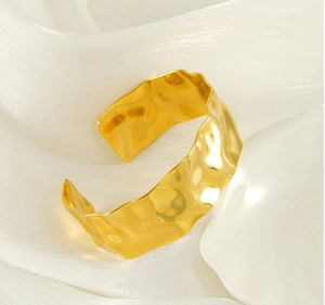 Detail of 18K gold-plated stainless steel cuff with hammered wave texture on white silk