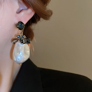 Macro detail of Baroque pearl drop earrings with dark grey gemstones worn by a model